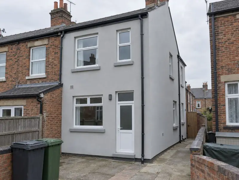Rear of a Victorian terraced house finished in pale grey insulated render with bins in the yard