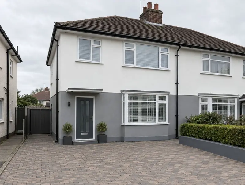 Semi-detached house with a white upper floor and grey render plinth, black downpipes and a block-paved drive